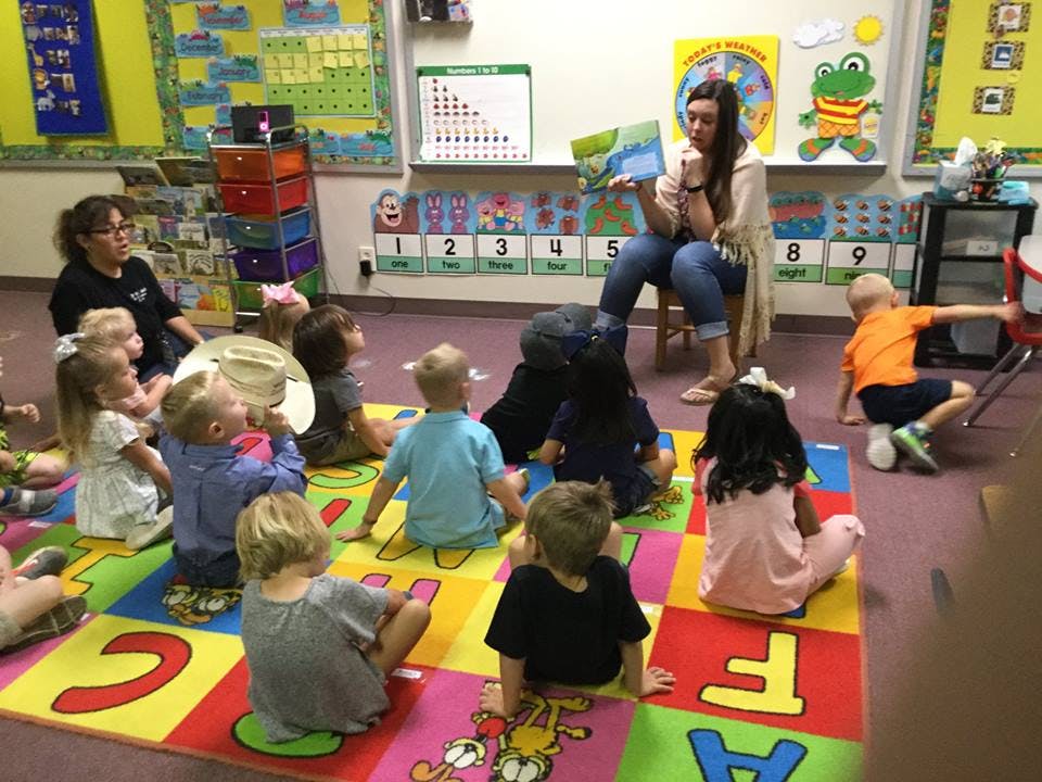 Adult reading a book to children sitting on a colorful alphabet mat in a classroom