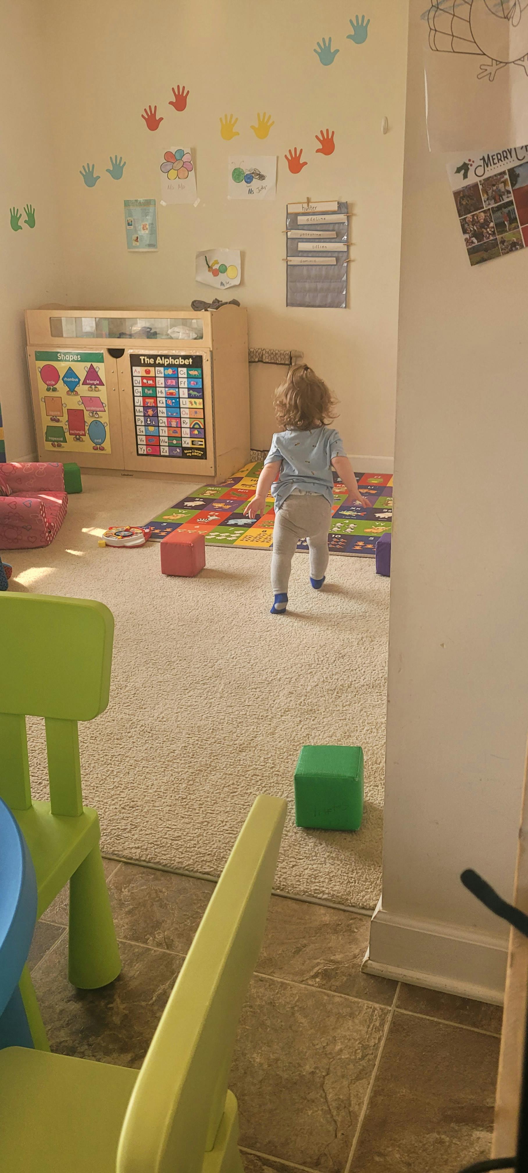 Child walking on a colorful playmat in a room with handprint decorations