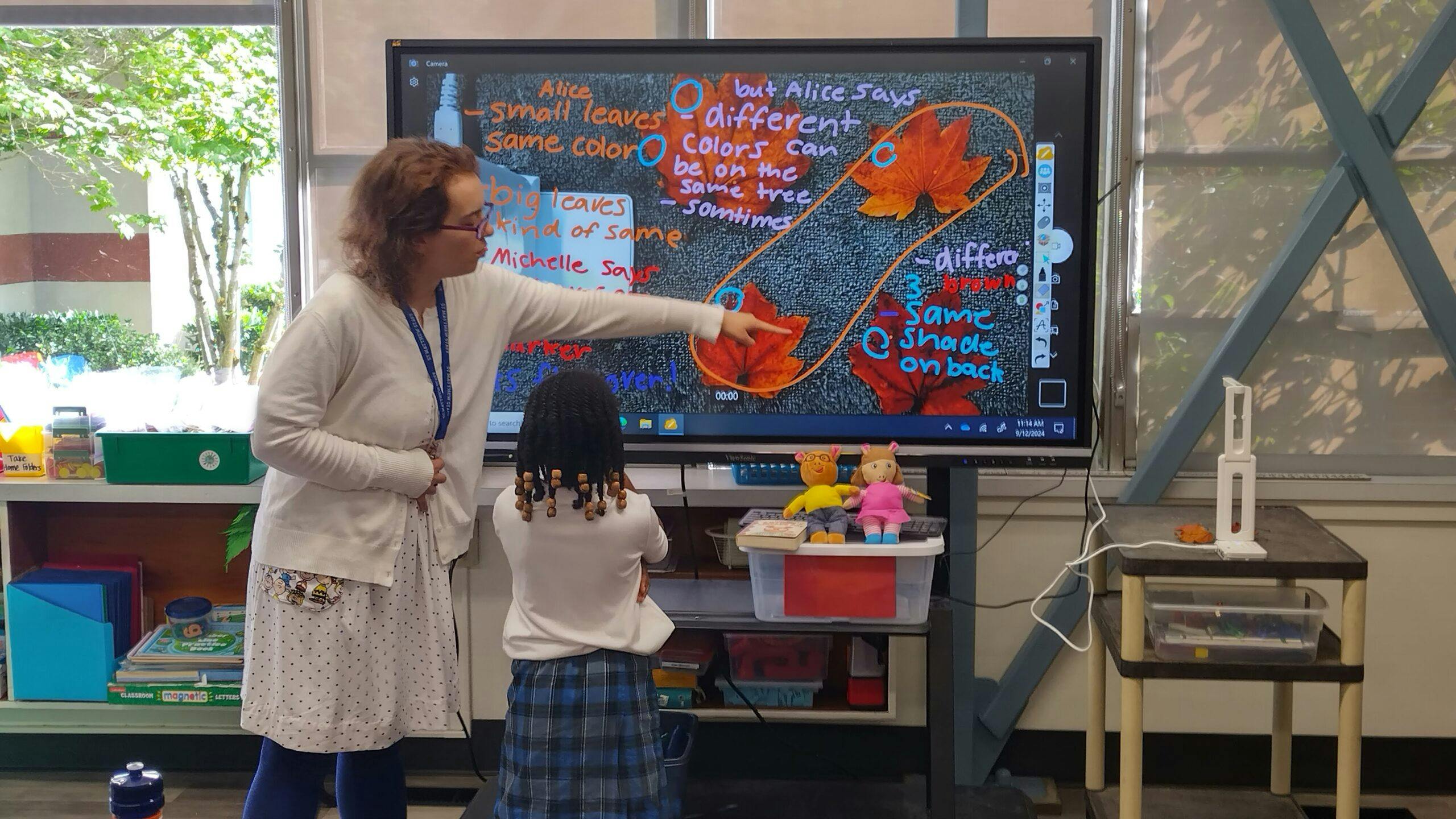 Person pointing at a large screen with a child in front of it