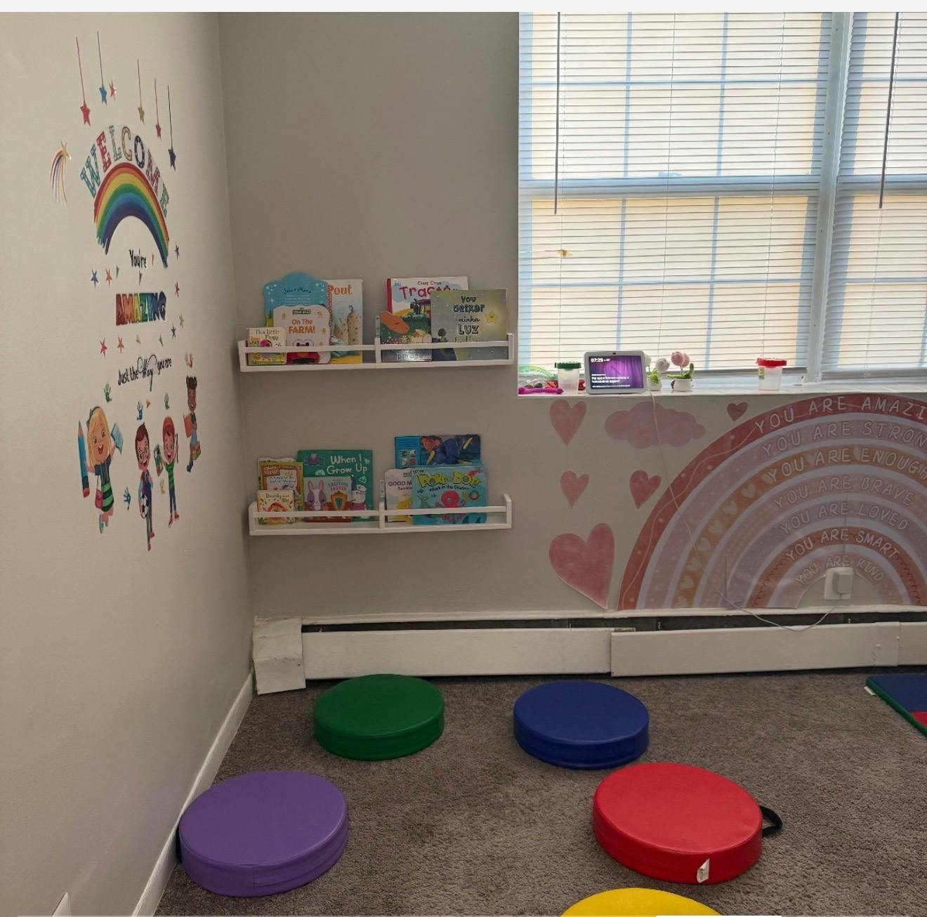 Children's room with rainbow wall decor, bookshelves, and floor cushions
