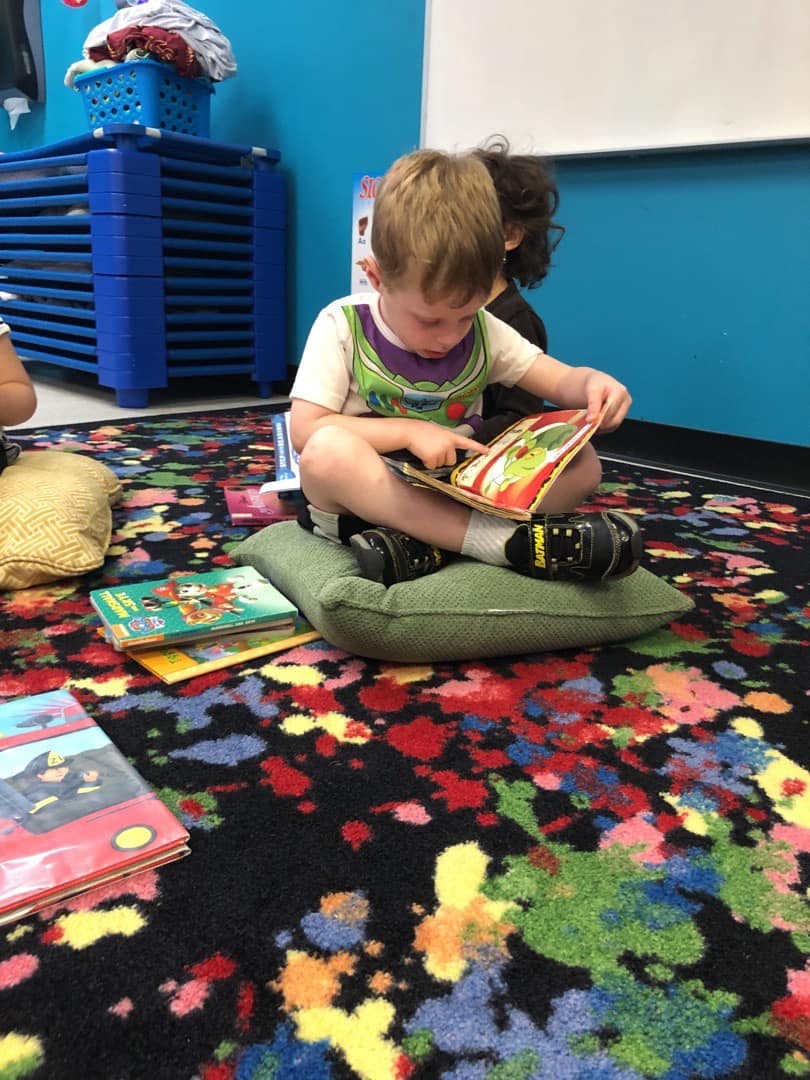 Child sitting on a pillow and reading a book in a classroom