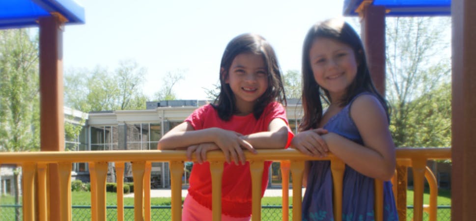Two children standing behind a yellow railing on a playground