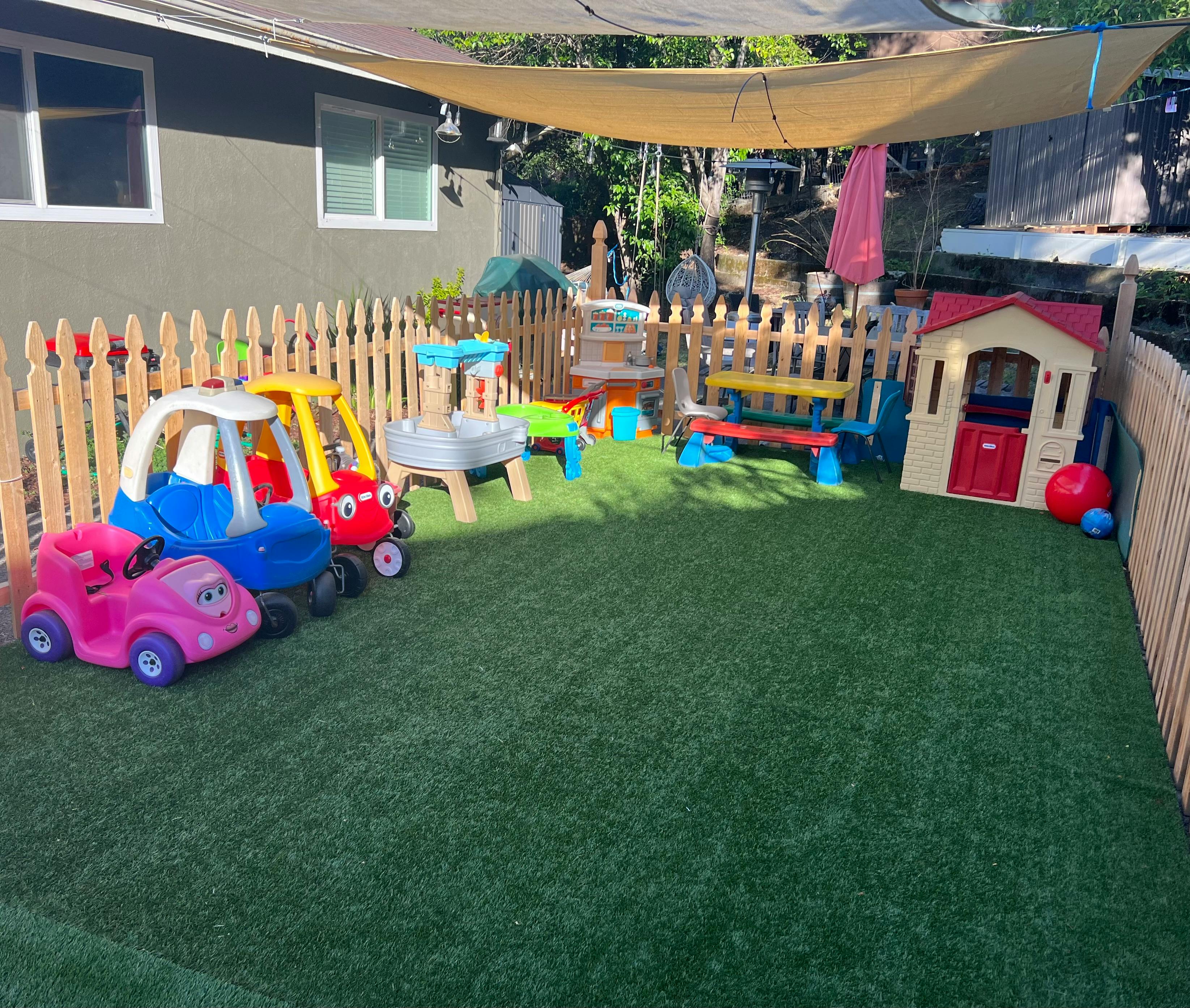 Outdoor play area with toy cars, playhouse, and fence