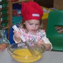 Child in red hat whisking liquid in a bowl