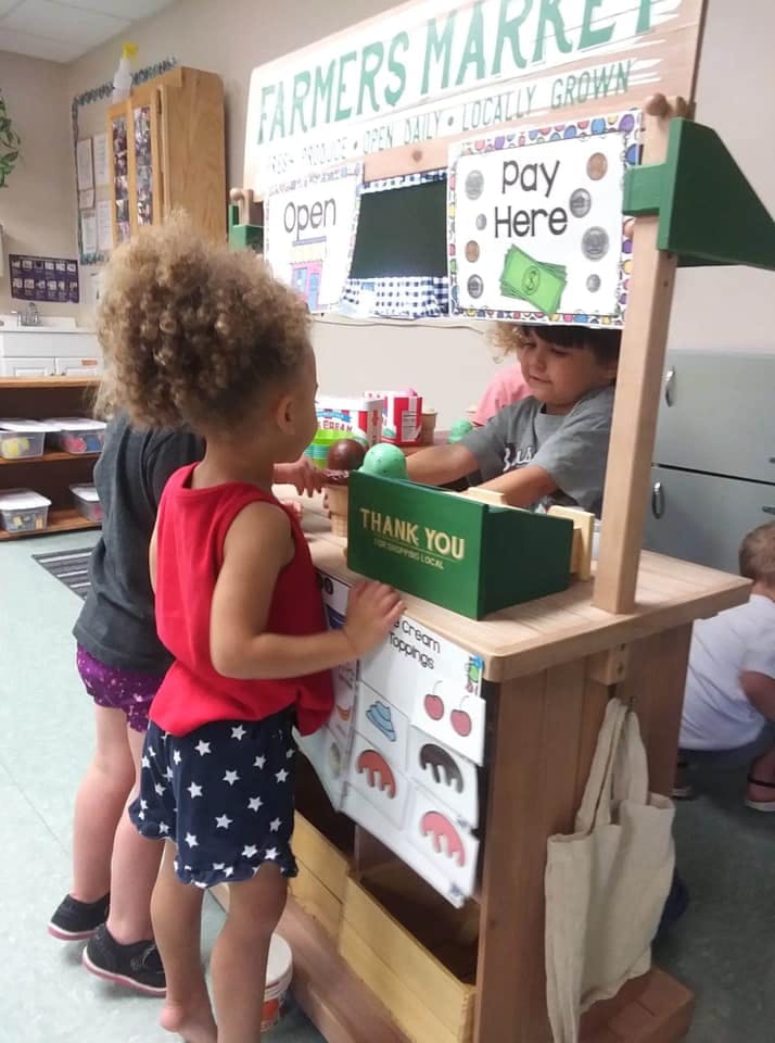 Two children playing at a toy farmers market stand