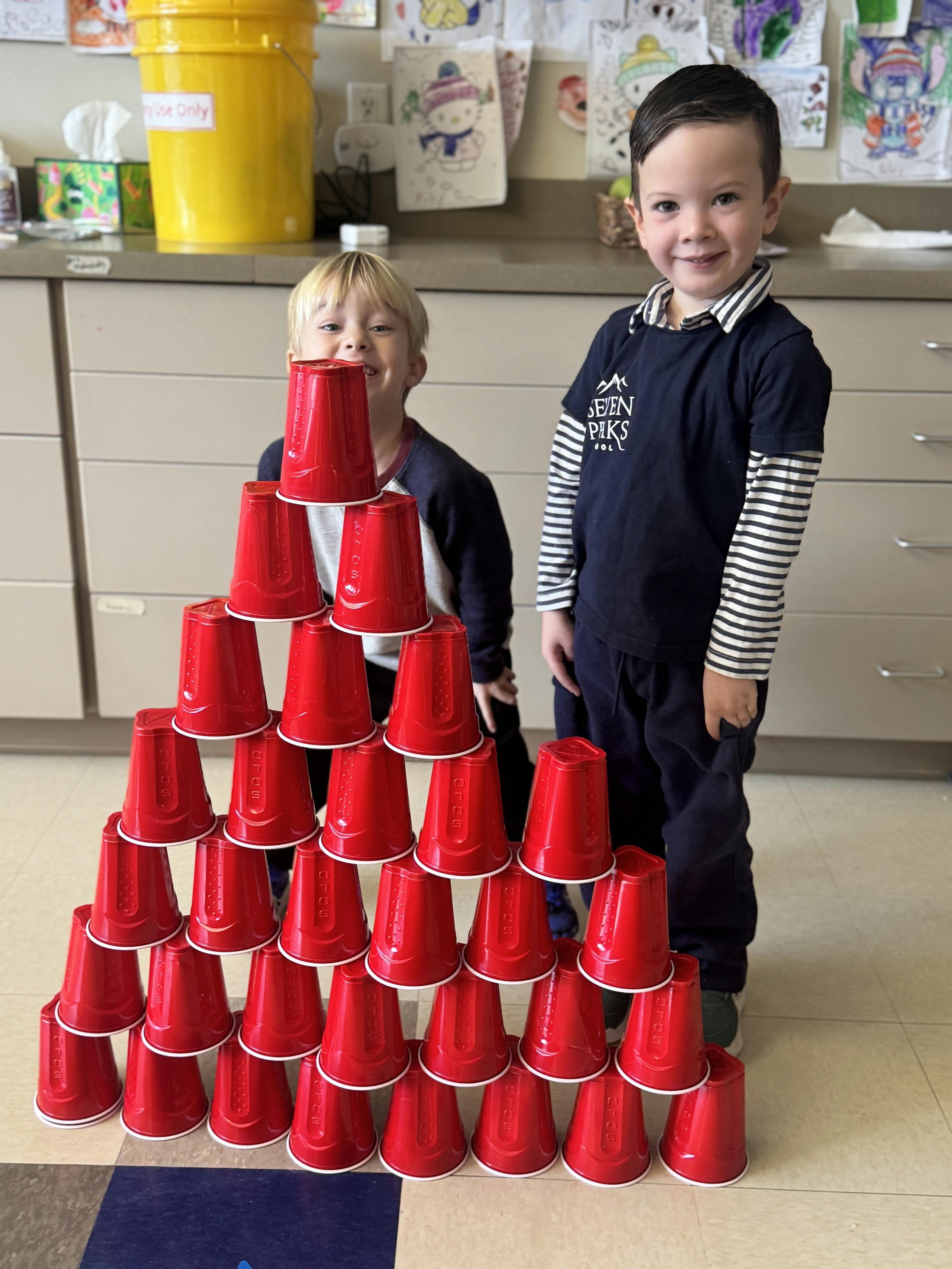 Two children standing behind a large pyramid of red plastic cups