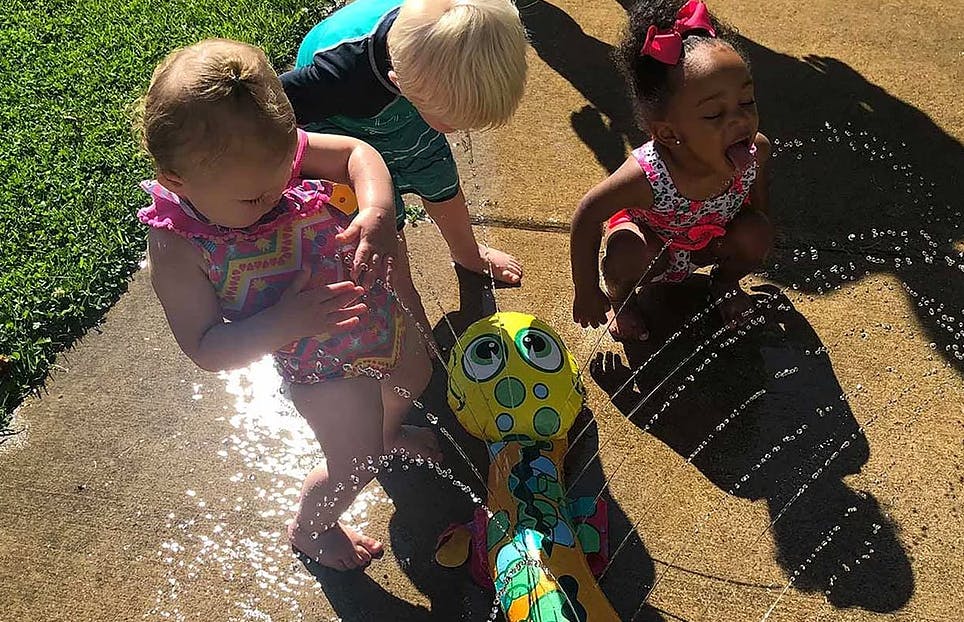 Three children playing with a sprinkler toy on a sunny day