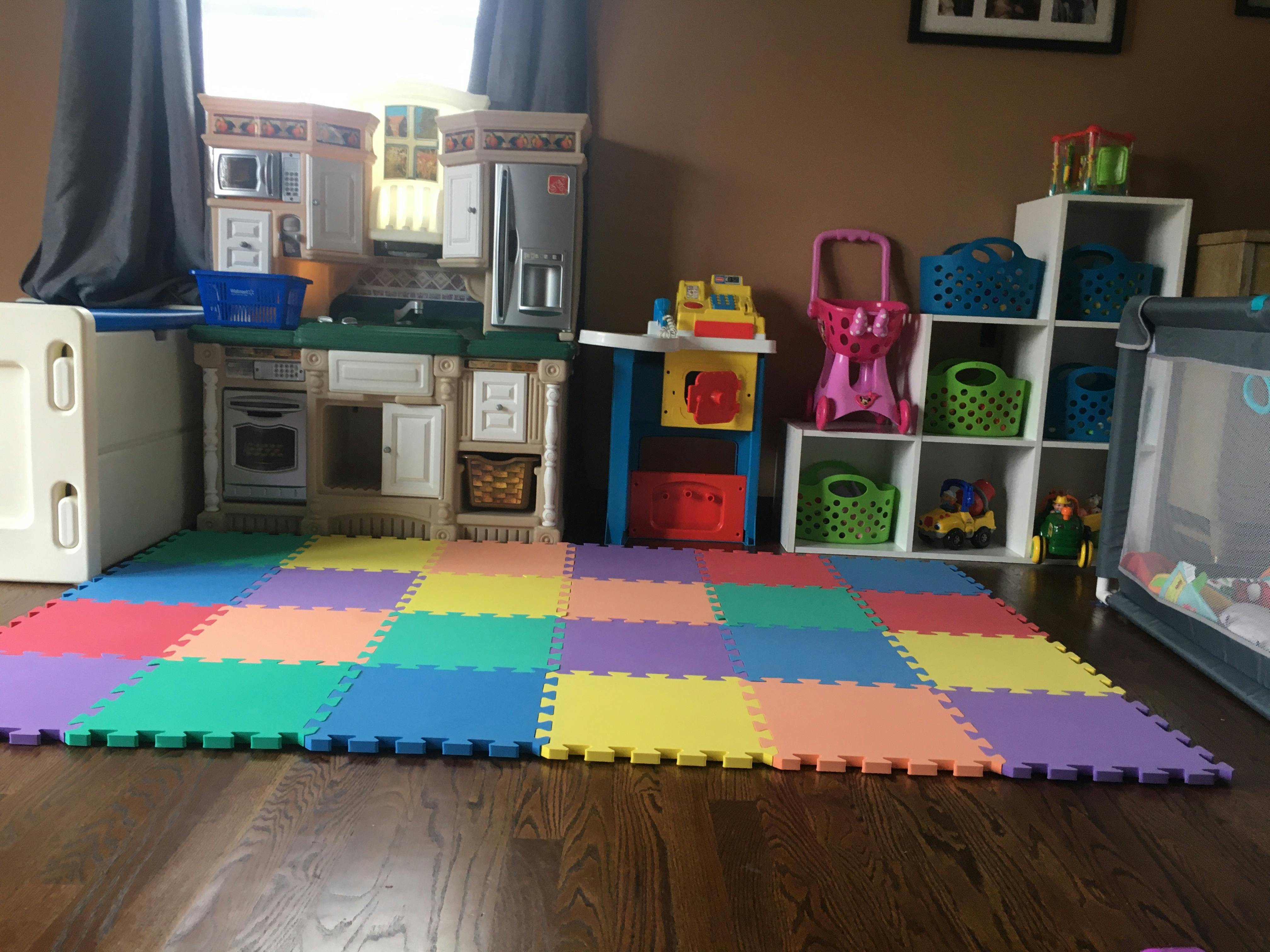 Playroom with a colorful foam mat, toy kitchen, and shelves with shelves of toys