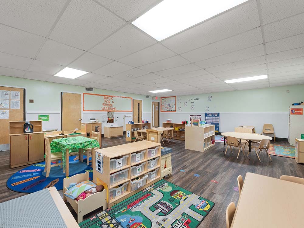 A colorful empty classroom with children's tables, rugs, and storage units