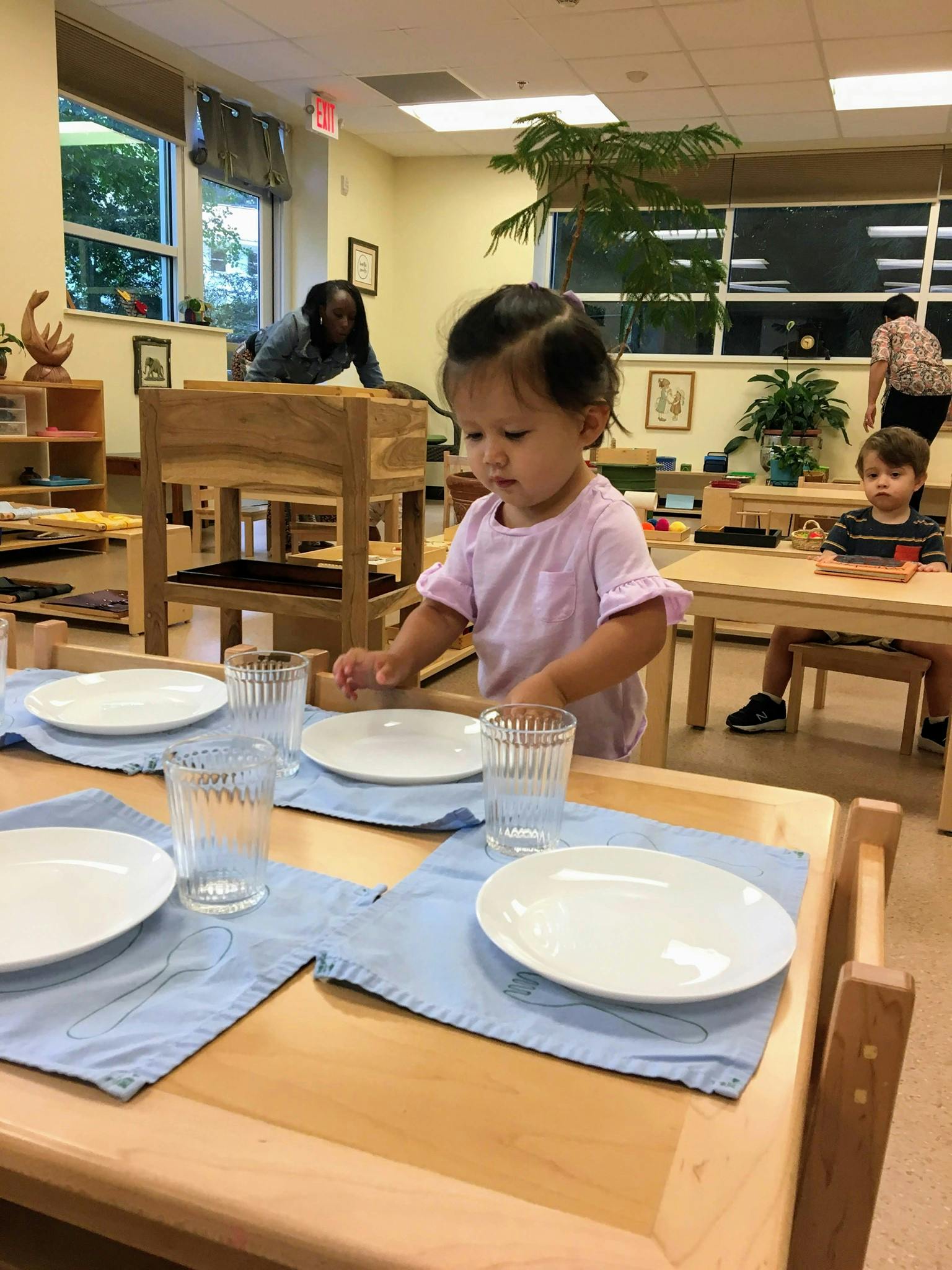 Child setting a table with plates and glasses in a classroom