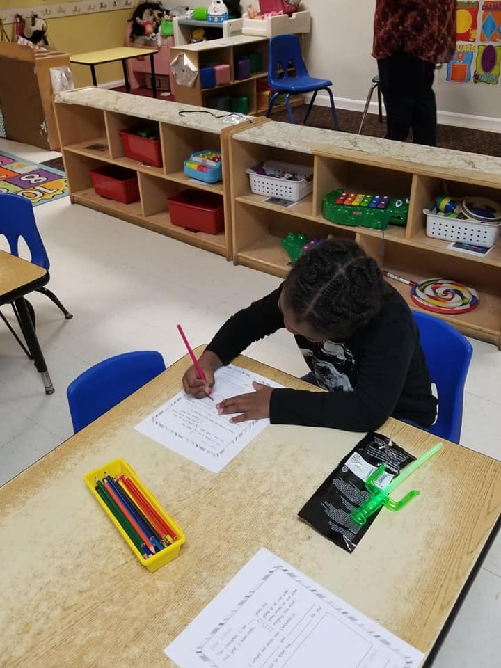 Child writing on paper at a desk in a classroom