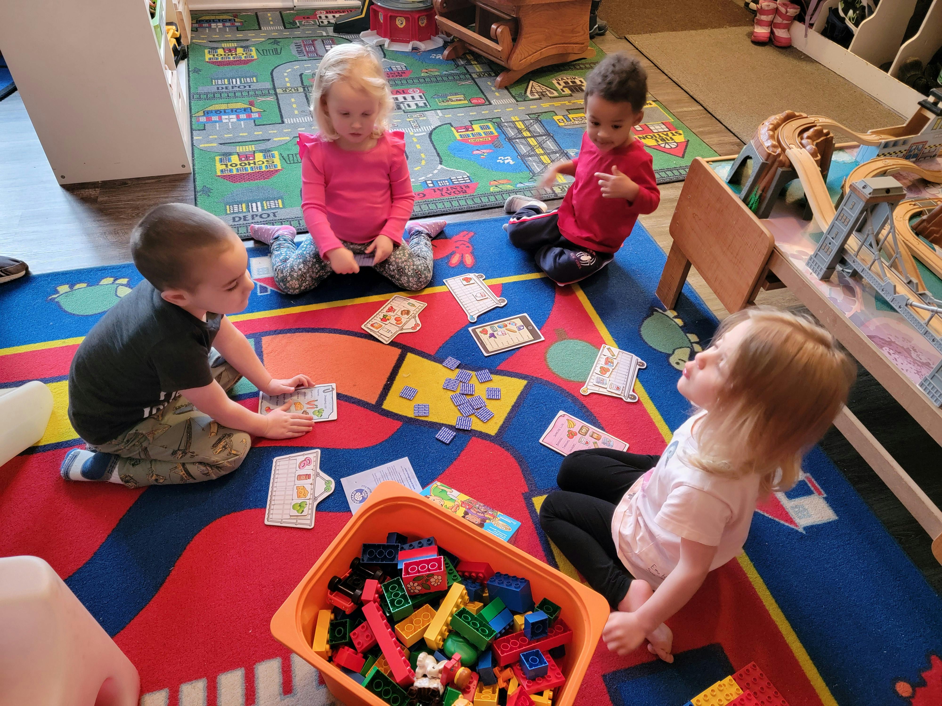 Four children playing with cards and blocks on a colorful rug