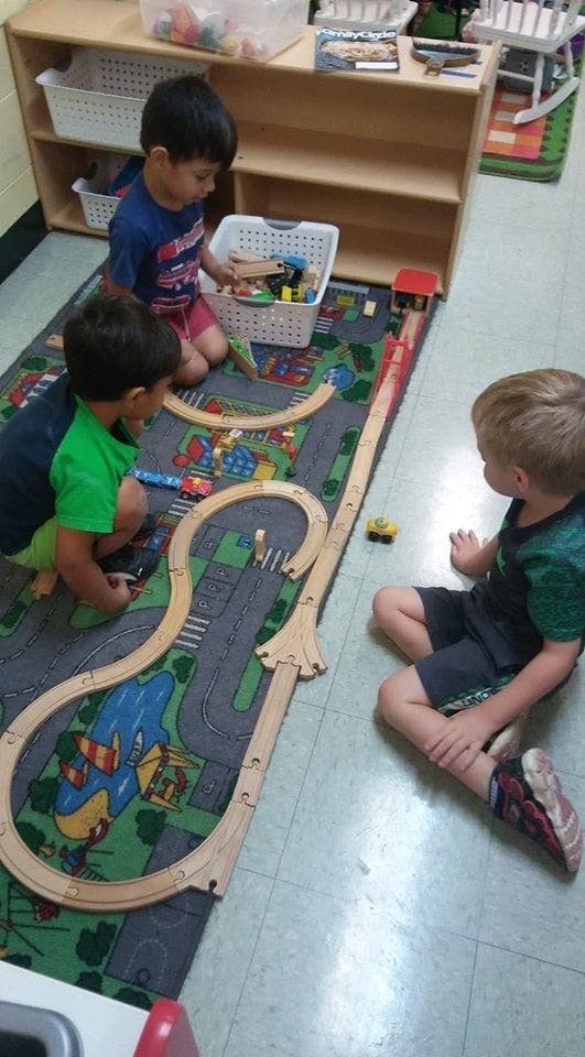 Three children playing with a wooden train set on a rug