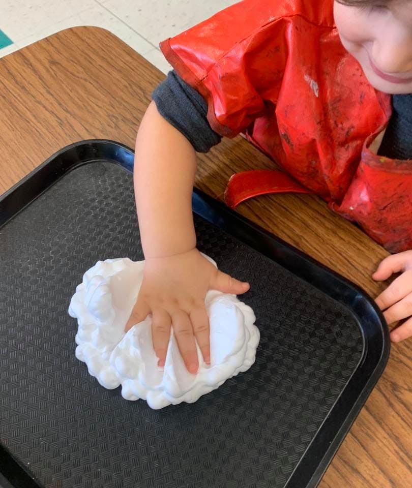 Child's hand pressing into white foam on a black tray
