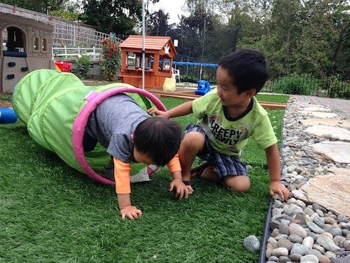 Two children playing with a green tunnel on grass