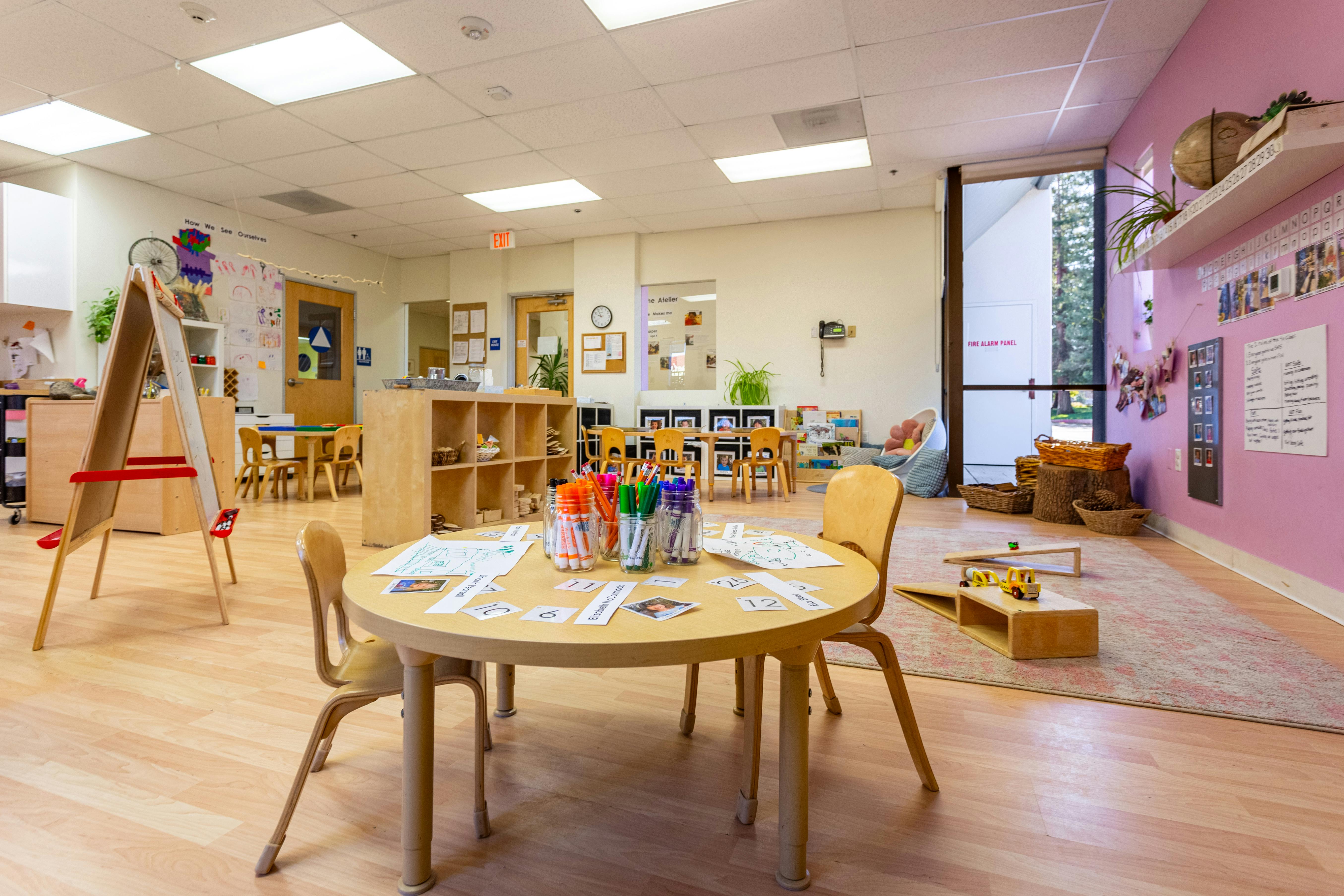 Empty classroom with small tables and chairs, art supplies on a round table