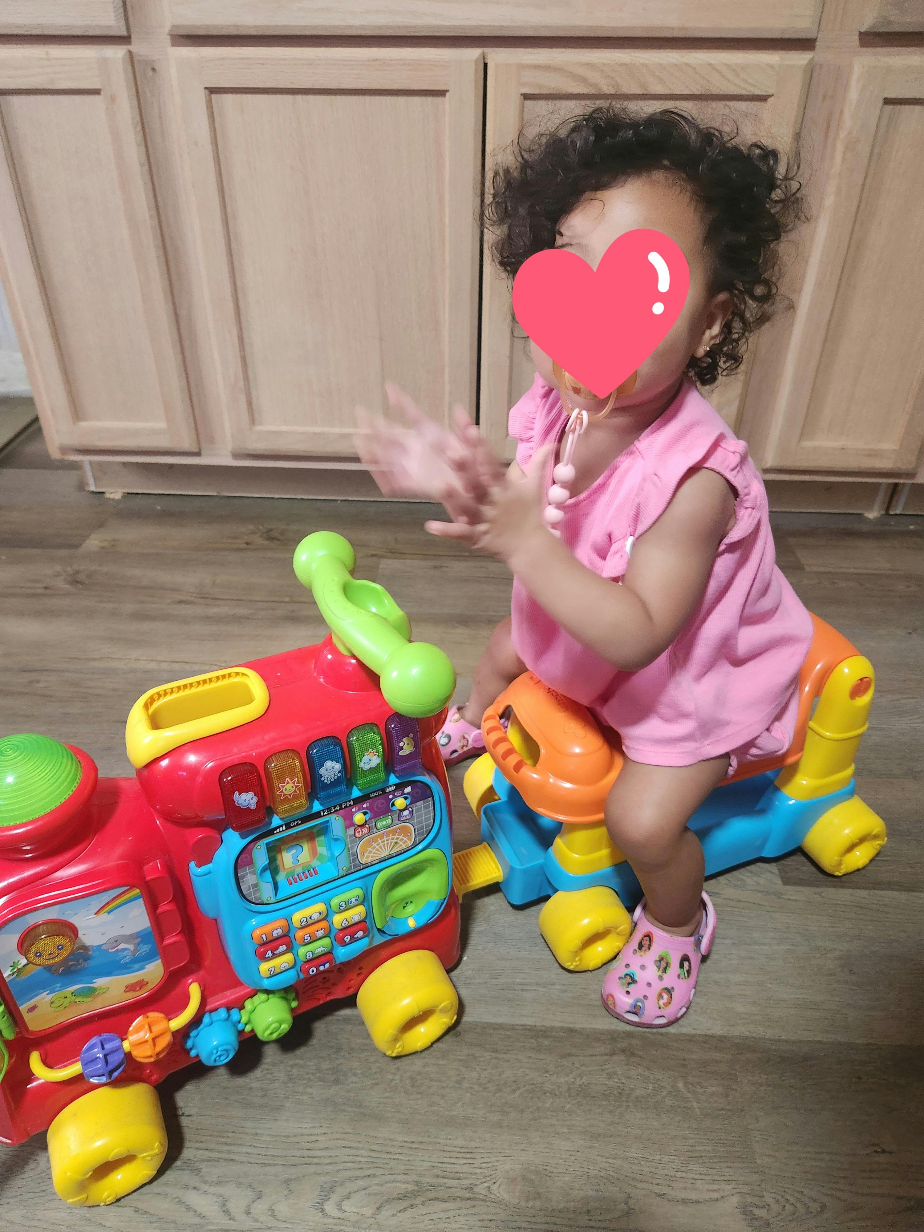 Child riding a colorful toy train and clapping hands