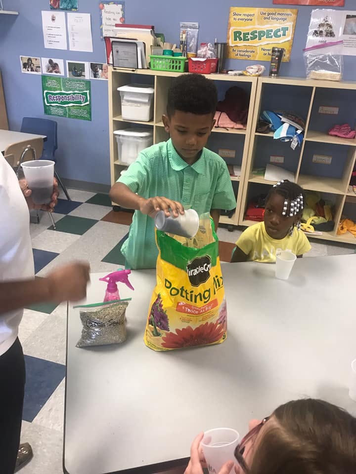 Child pouring potting mix from a cup into a bag of potting mix