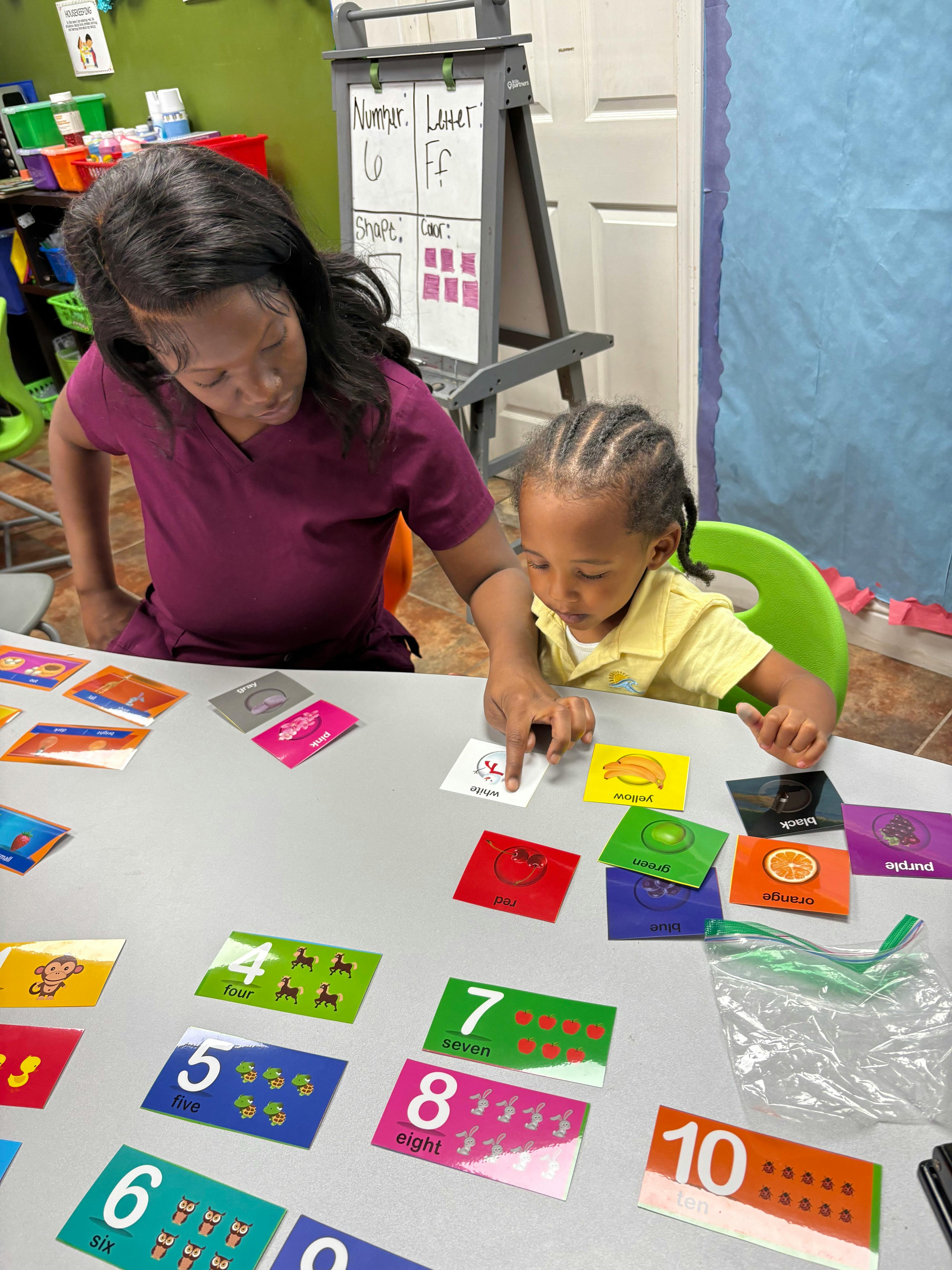 Adult and child pointing at learning cards on a table in a classroom