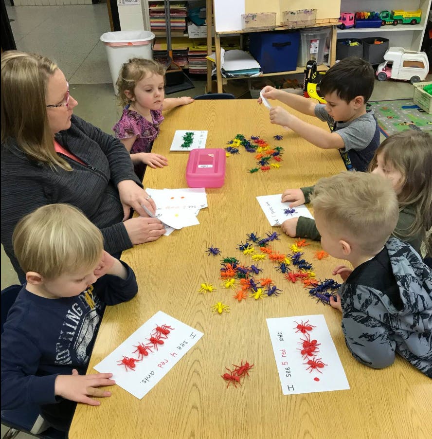 Adult and children at a table with colorful insect counters and worksheets