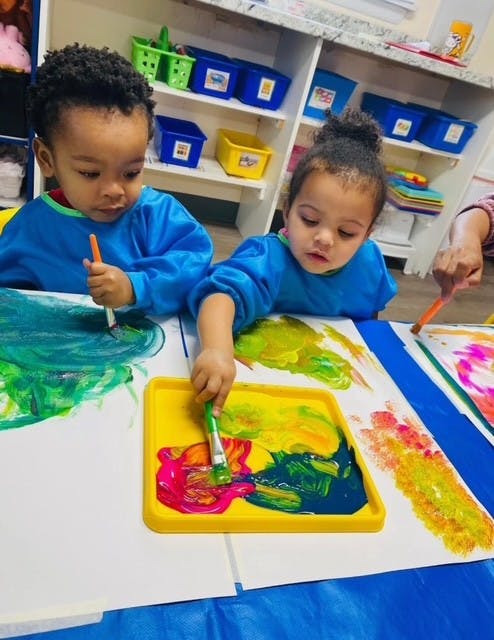Two children painting with brushes on paper at a table