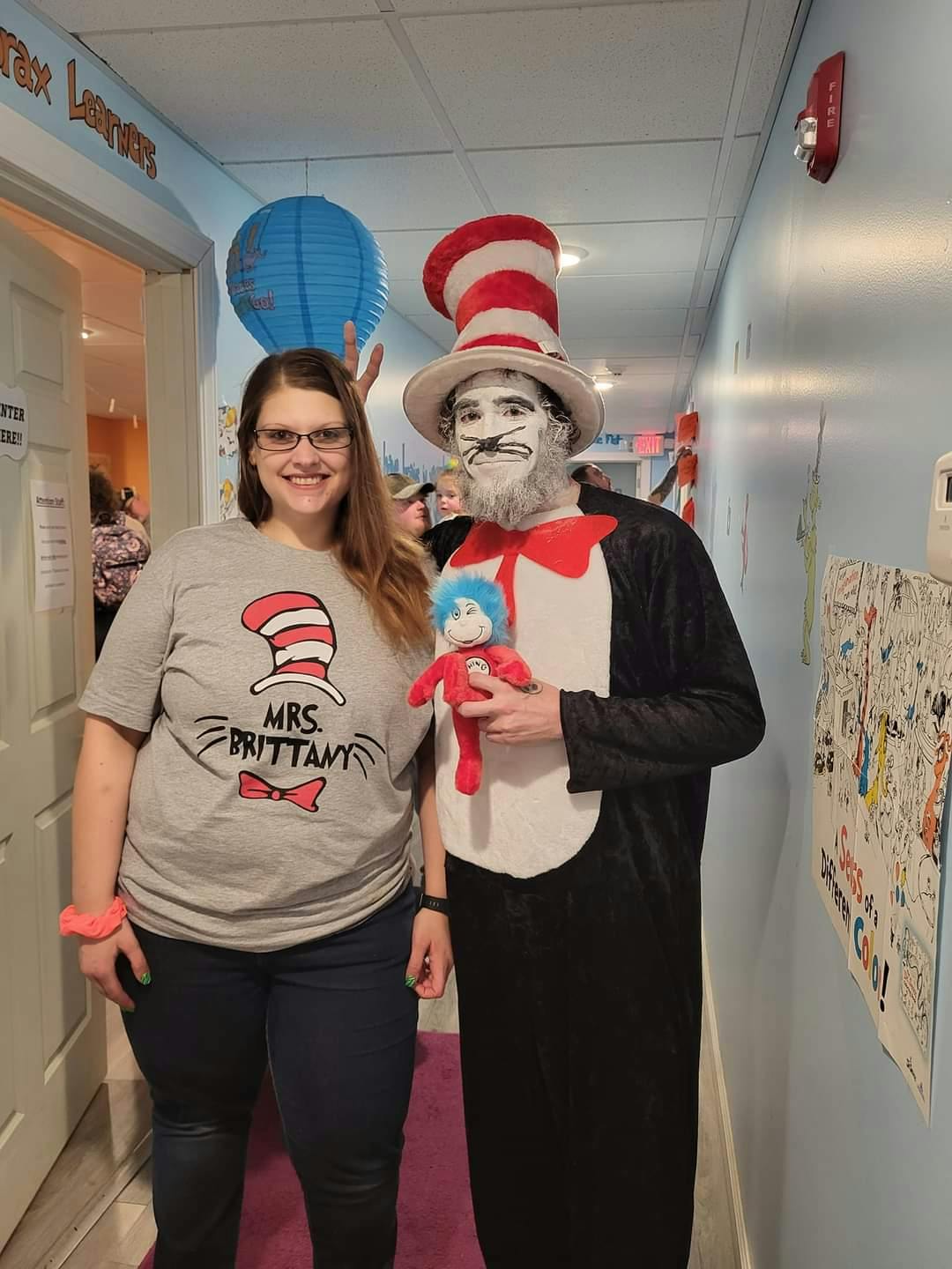 Person in Cat in the Hat costume holding a doll next to a person in a themed shirt