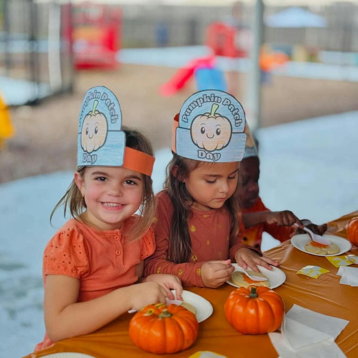Children wearing Pumpkin Patch Day paper hats sitting at a table with pumpkins