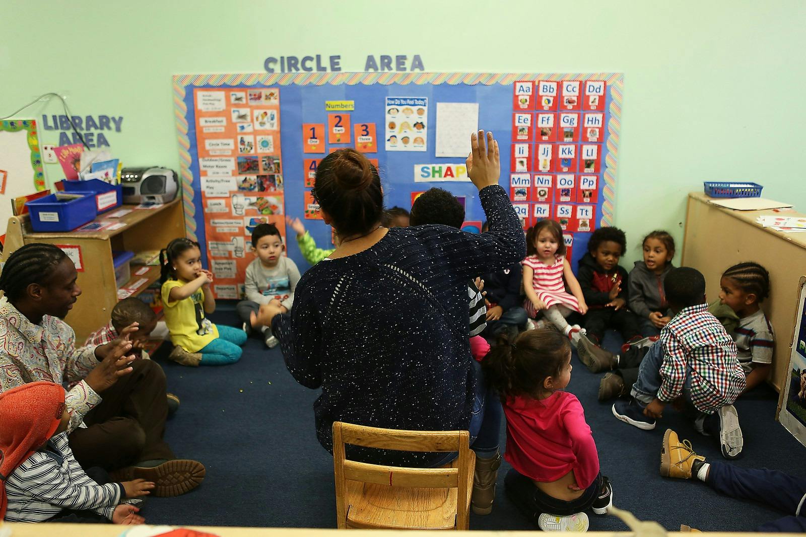 Adults and children sitting on the floor in a classroom, "CIRCLE AREA" classroom
