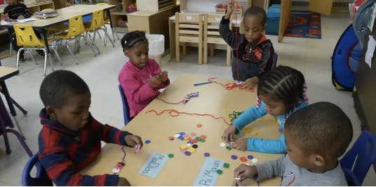 Children playing with colorful pieces on a table in a classroom