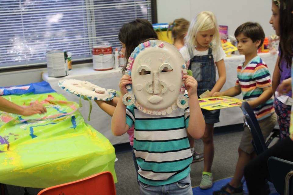 Child holding up a paper plate mask in a classroom