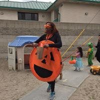 Person in pumpkin costume holding a treat bag, child in background