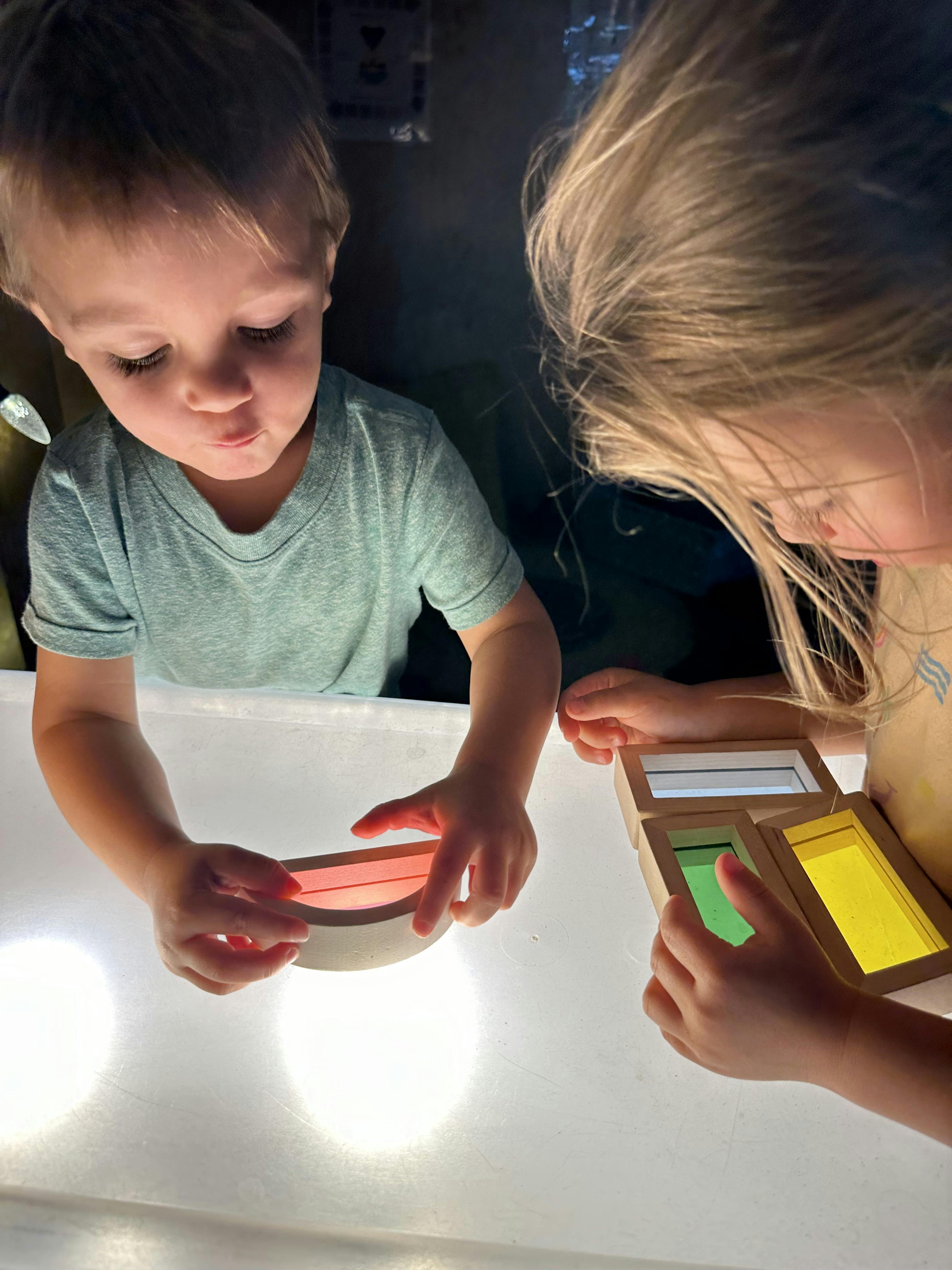 Two children playing with colorful blocks on a light table