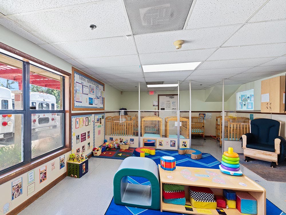 A classroom with cribs separated by clear partitions, toys, and a window