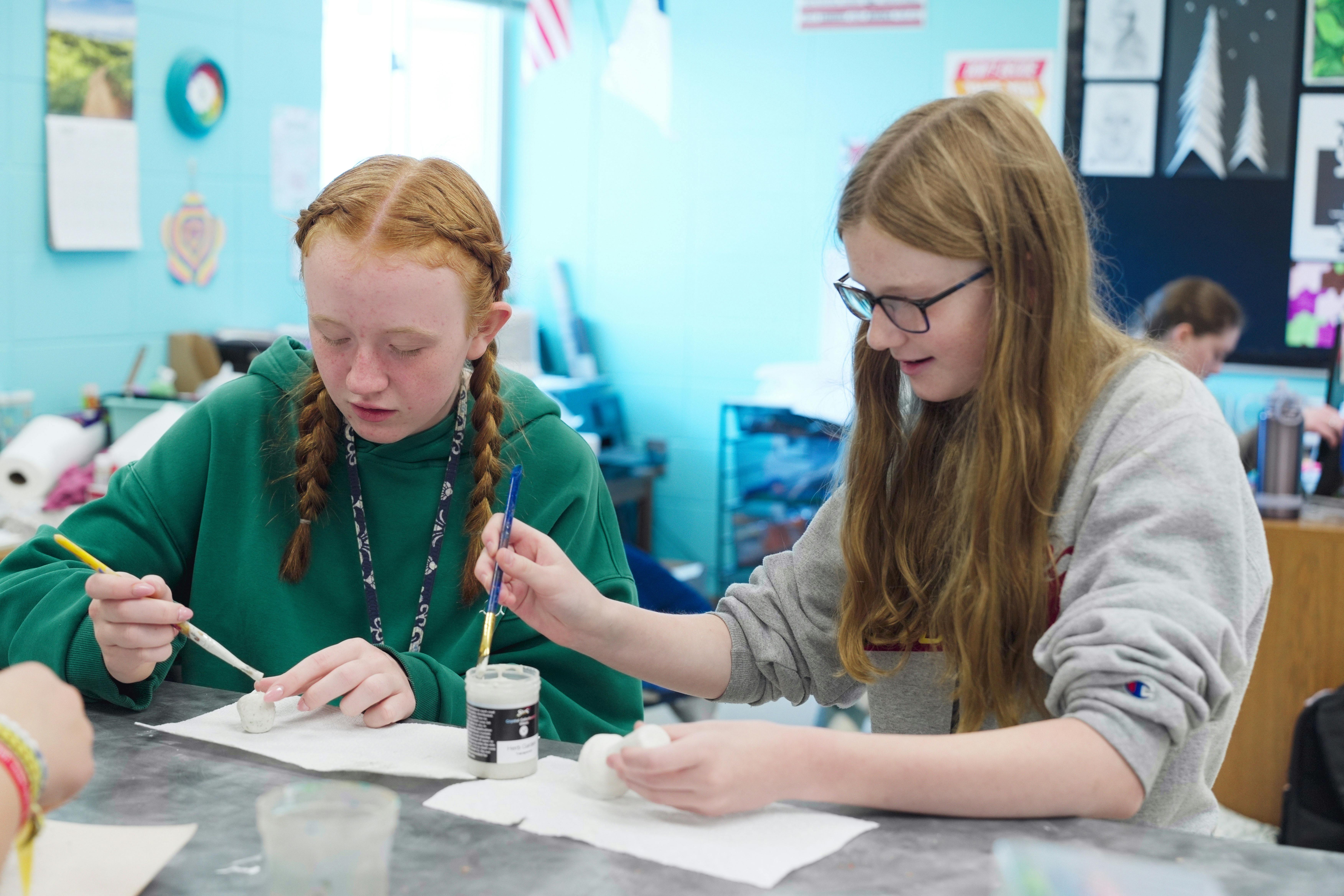 Two teens painting small objects in a classroom