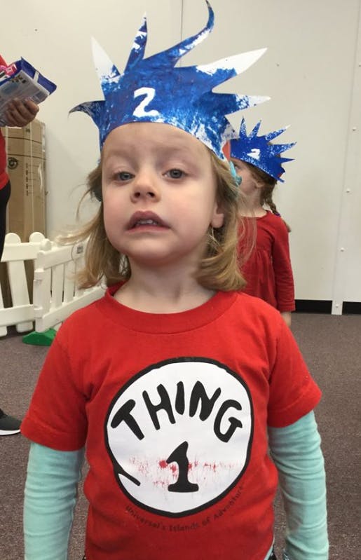 Child wearing a red shirt with "Thing 1" and a blue crown with "2"