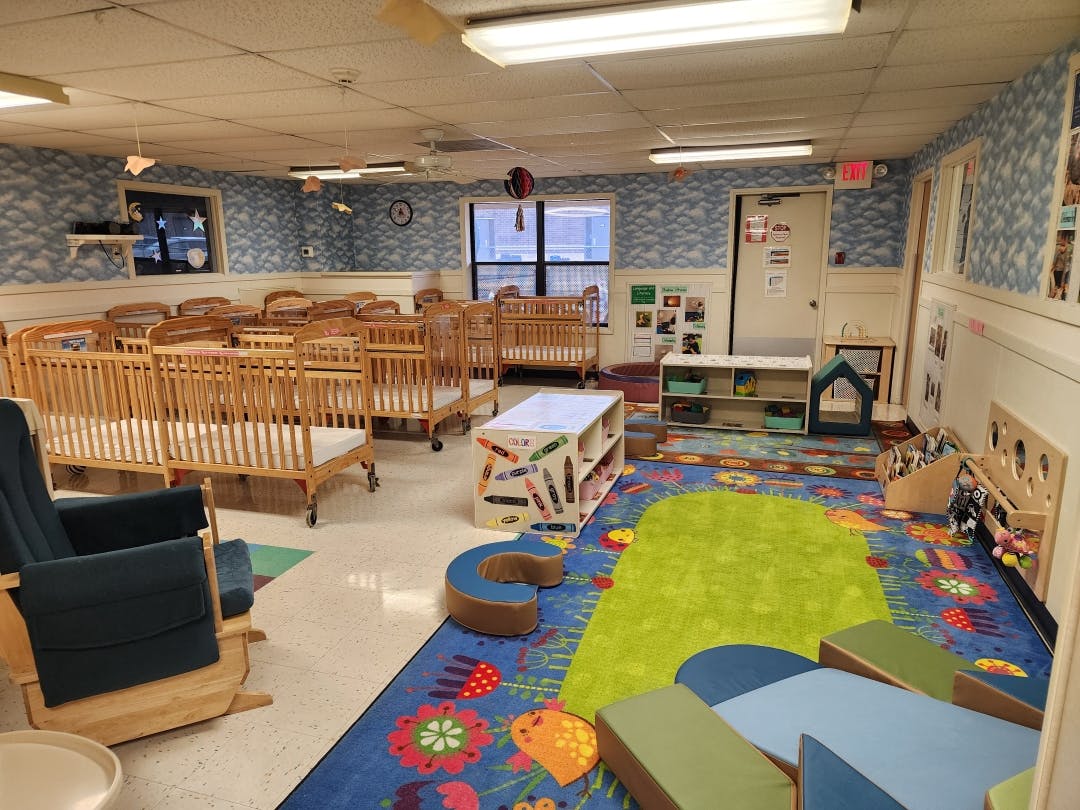 Classroom filled with multiple cribs, a colorful rug, and child-sized furniture