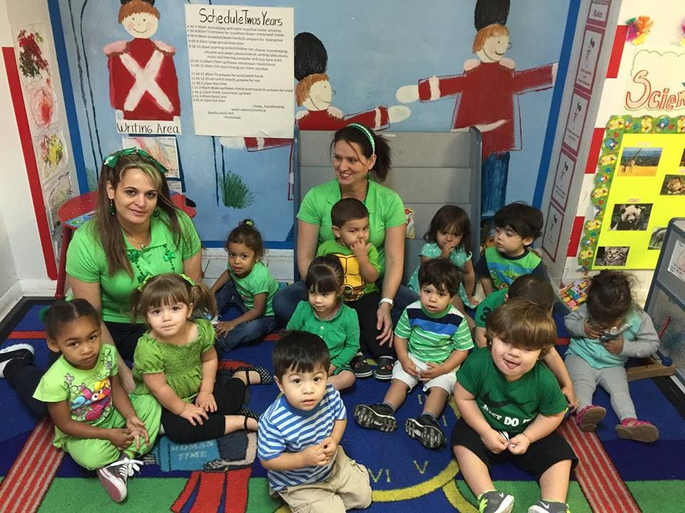 Two people with a group of children sitting on a rug in a classroom