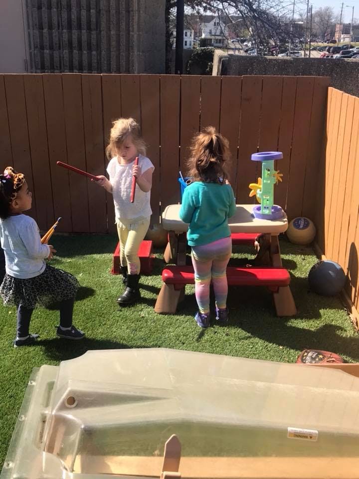 Three children playing with toys in a fenced outdoor area