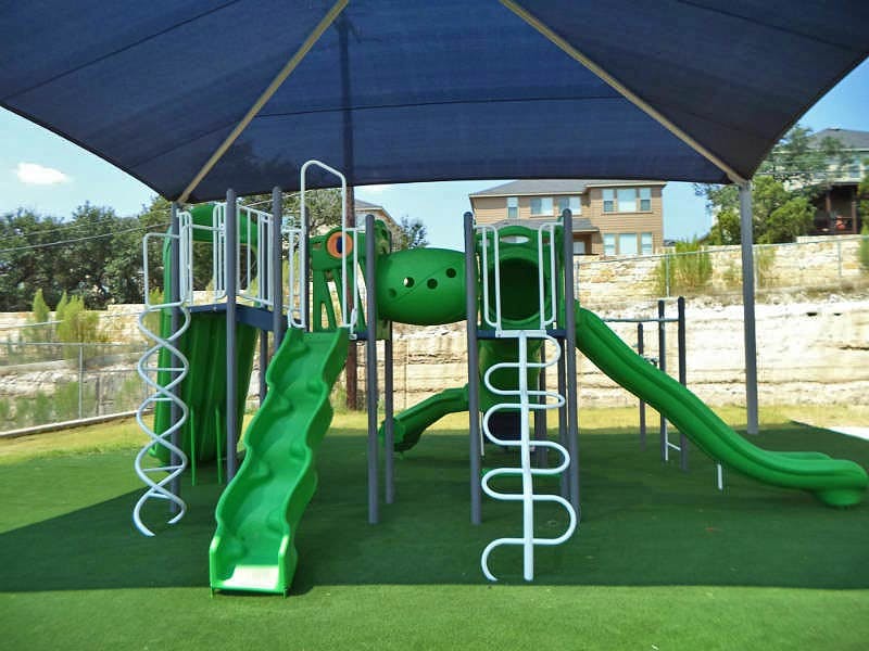 Green playground structure with slides and climbing elements under a shade canopy