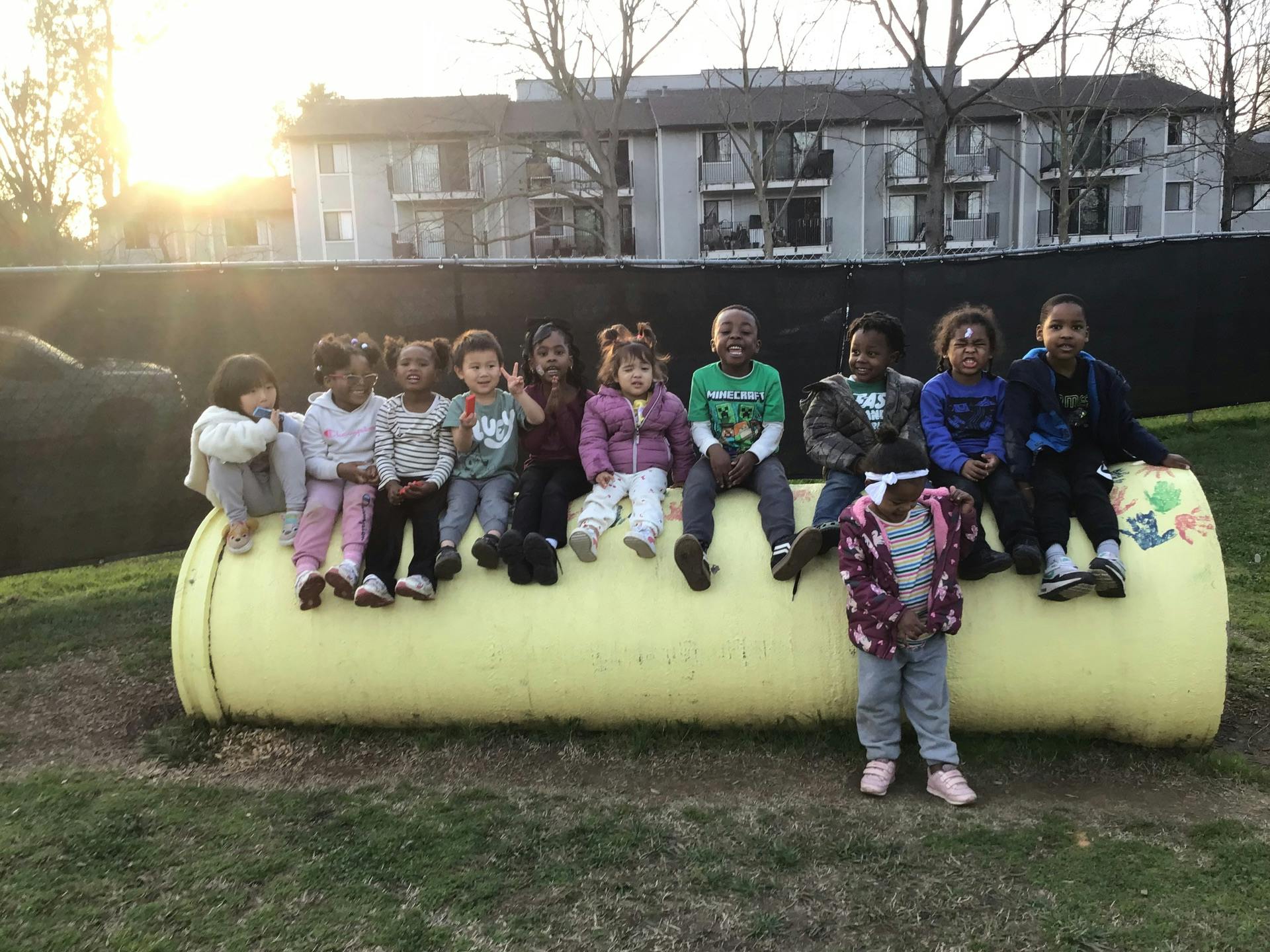 Group of children sitting on and standing by a large yellow pipe