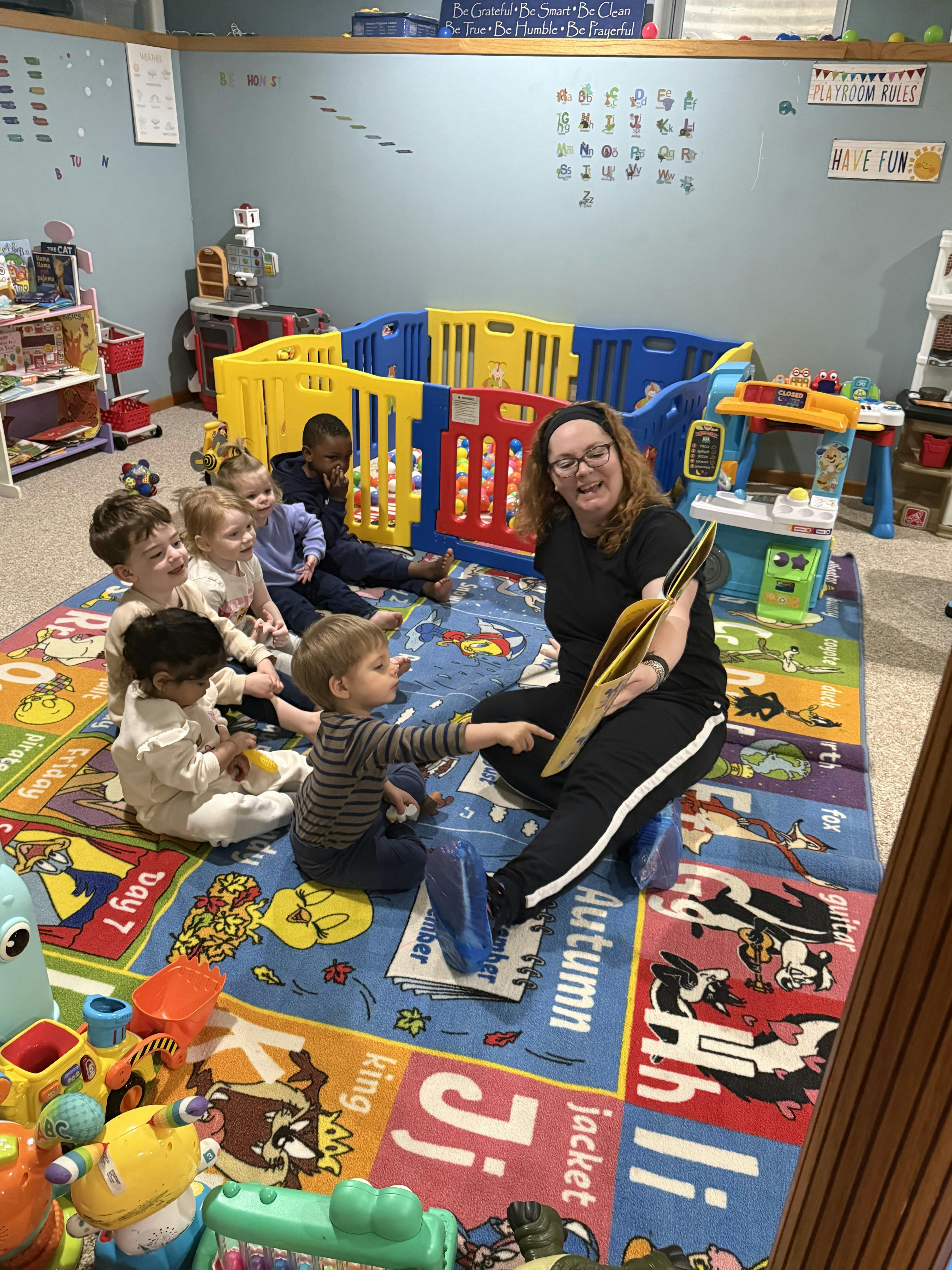 Adult reading a book to a group of children in a playroom