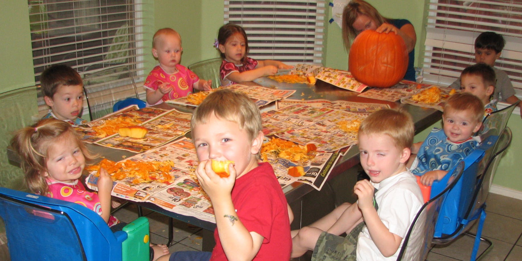 Children at a table with a person and a pumpkin