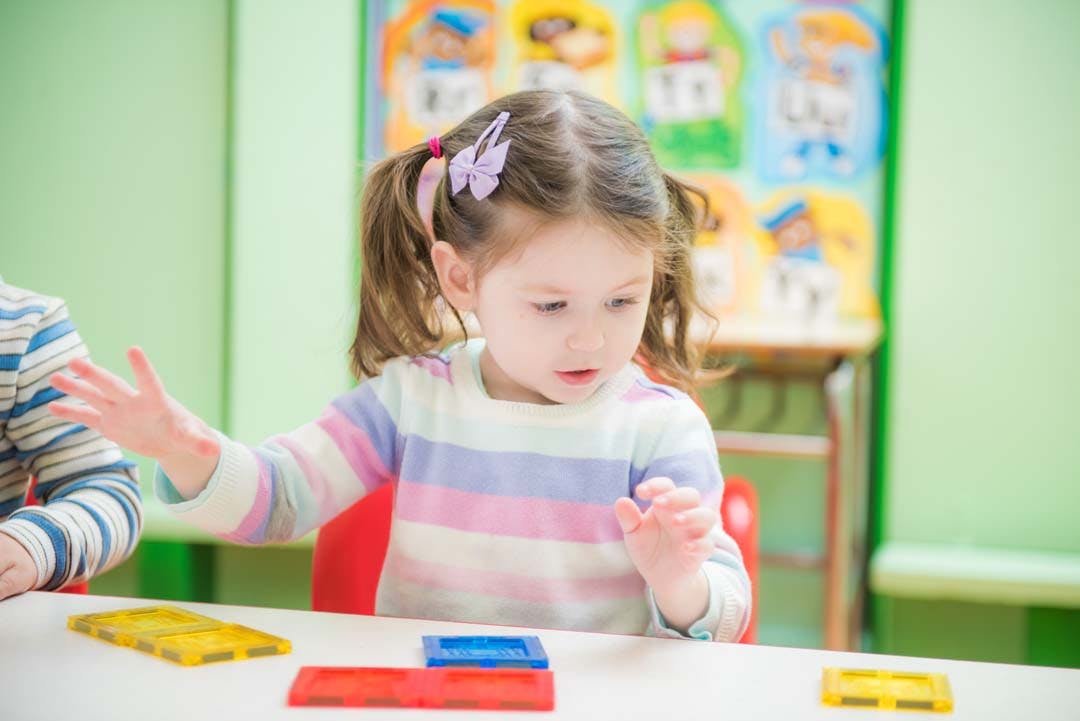 Child with pigtails playing with colorful blocks at a table