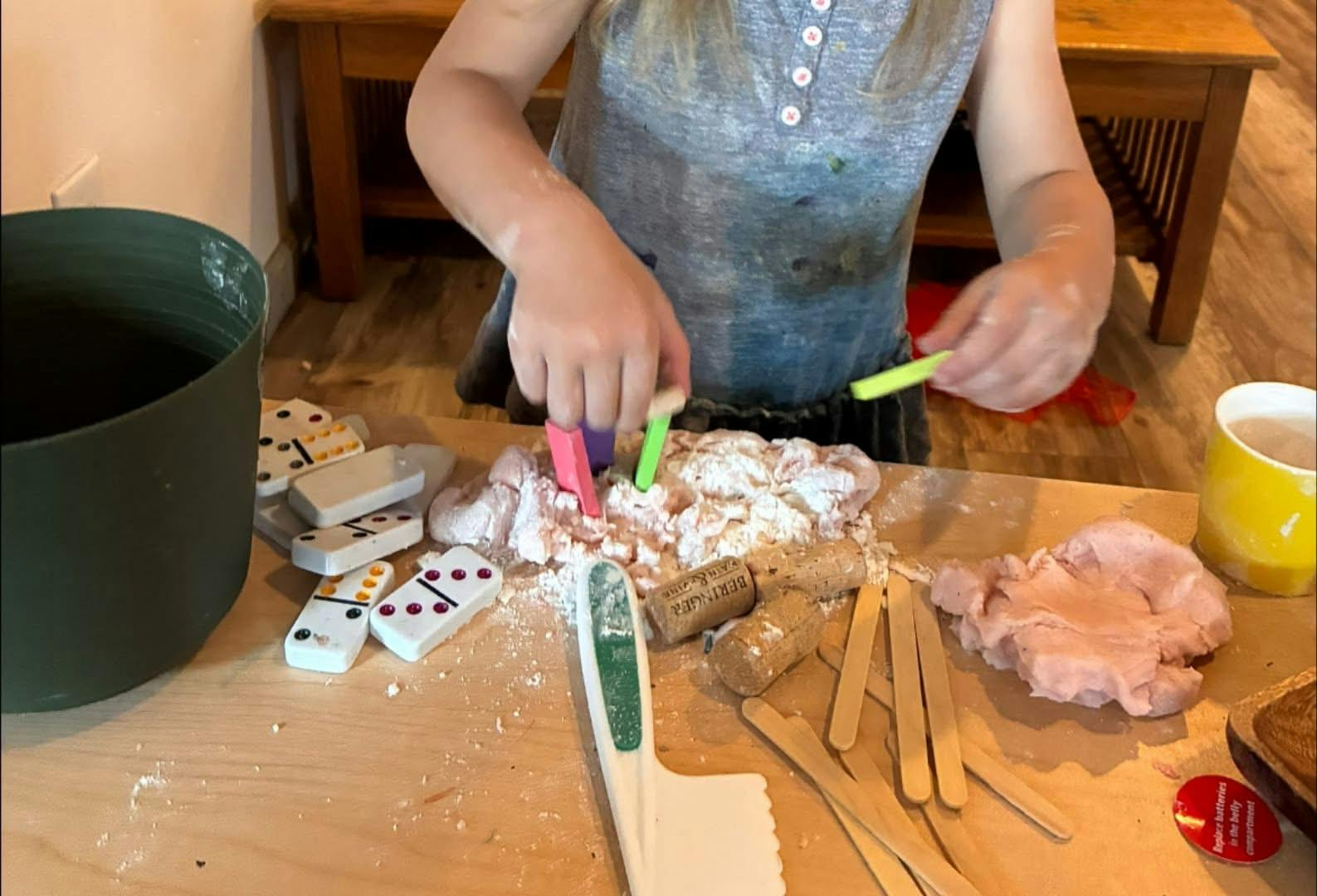 Child playing with dough, dominoes, and sticks on a table