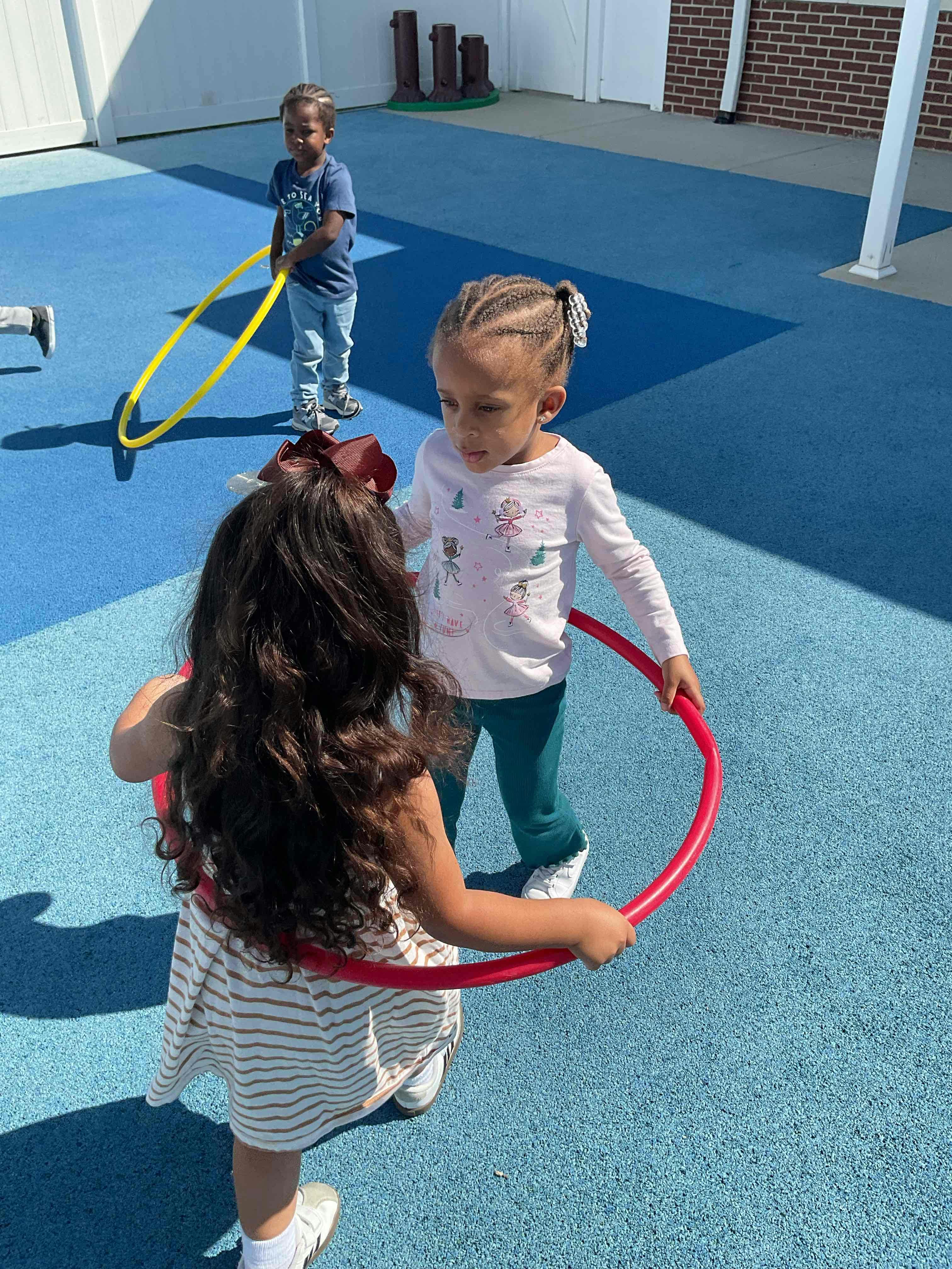 Two children playing with hula hoops on a blue surface