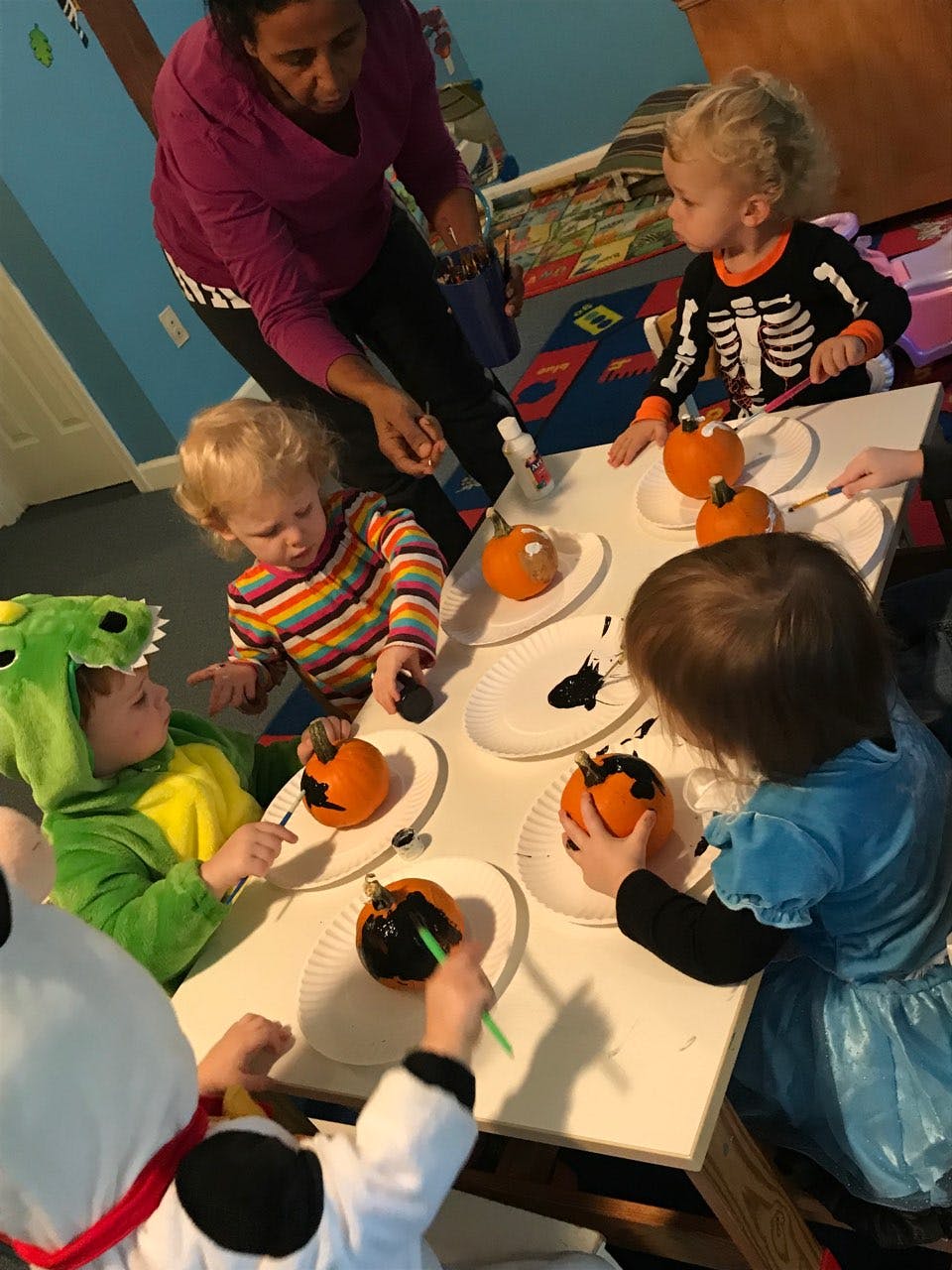 Adult supervising children painting small pumpkins at a table