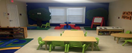 Classroom with small tables and chairs, play mats, and a window