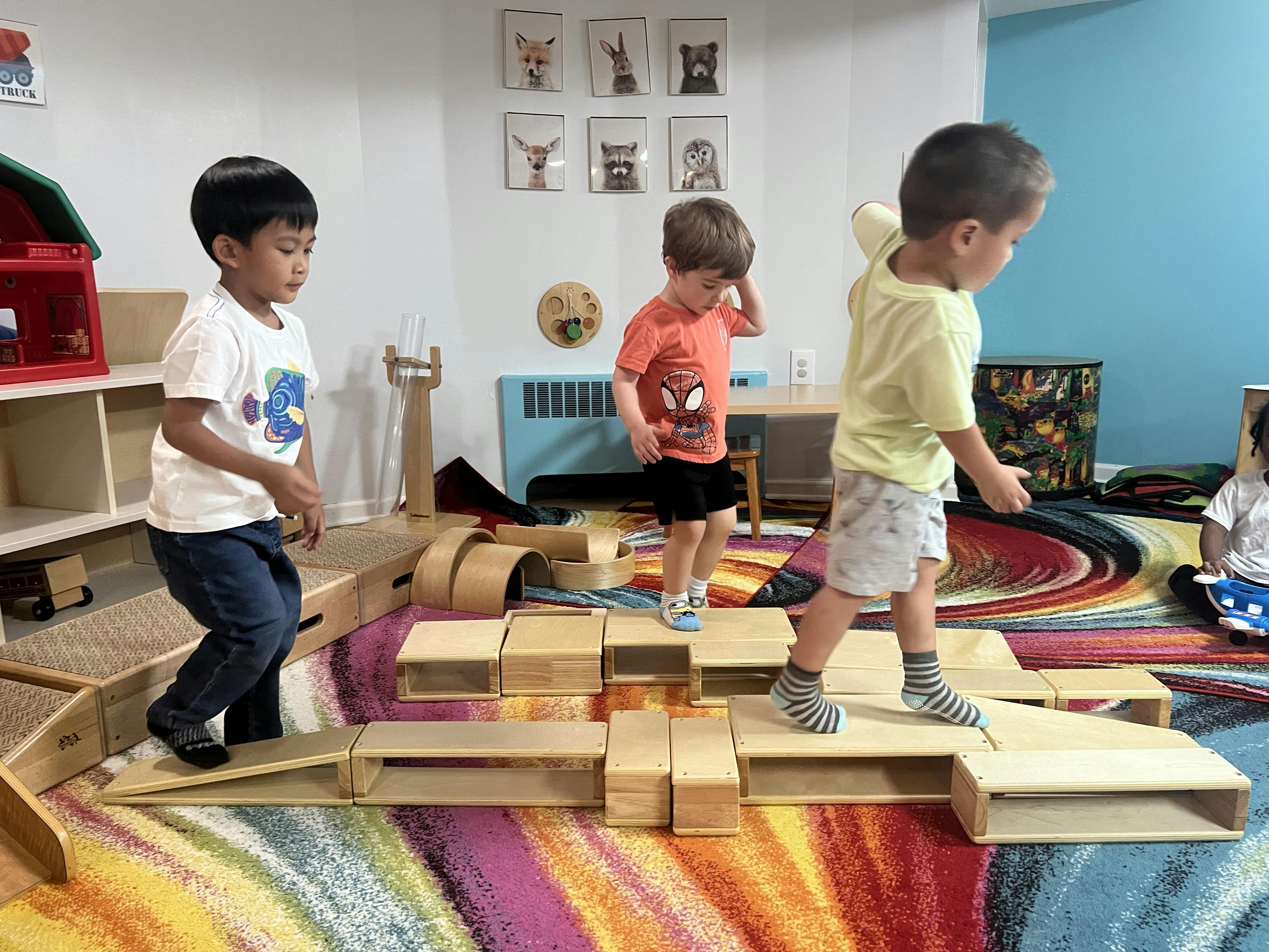 Three children playing on wooden balancing blocks in a classroom