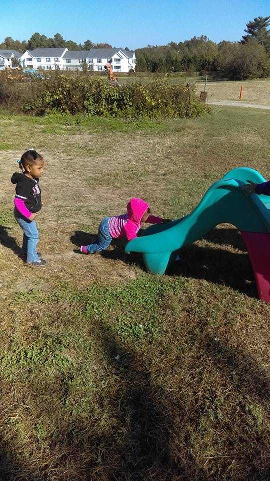 Child standing next to another child crawling onto a small slide