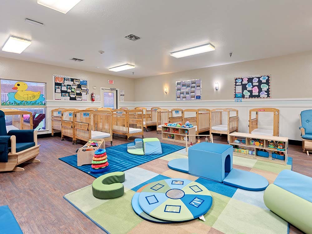 A room with multiple cribs, a rocking chair, and play mats with soft play equipment